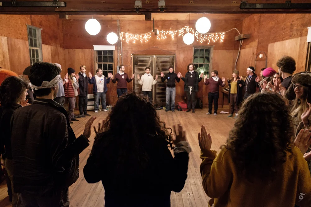 A circle of participants gathered in a warmly lit wooden hall